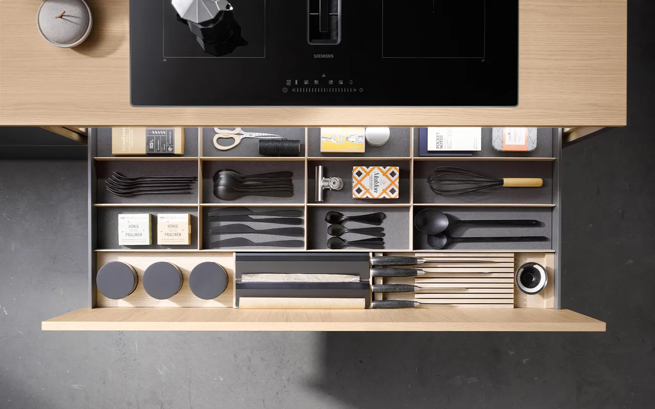 Übersichtlich sortierte Küchenschublade mit Besteck, Messern und Küchenutensilien. Hochwertiger Holzeinsatz für Ordnung und Stil in modernen Küchen.